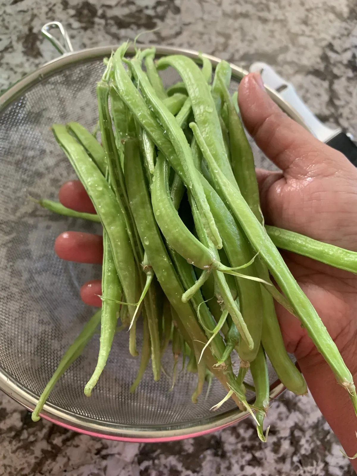 a person holding up some green beans in a glass bowl